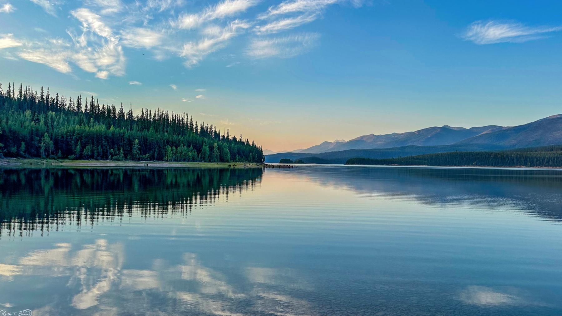 Mirror-still lake at dawn with forested shores